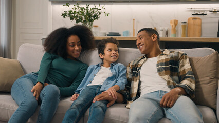 Relaxed tired African American family man dad male mother female woman little child boy son kid falling jumping on comfortable sofa couch rest celebrating own home rented relocation moving living room