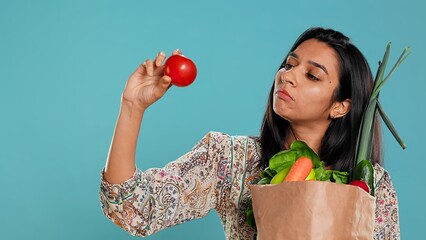 Woman with recycled paper bag in hands filled with vegetables testing quality, studio background....