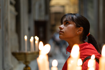 Young girl prayer in a church by candlelight