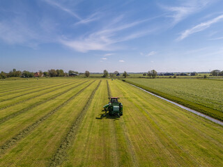 Aerial View: Tractor Gathering Rows of Grass into Piles on Farmland