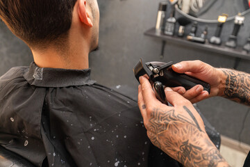   tattooed barber cutting the hair and beard of a young, dark-haired client.