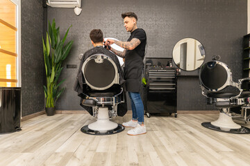 Fototapeta premium tattooed barber cutting the hair and beard of a young, dark-haired client.