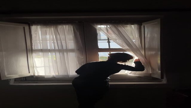 Mujer corriendo las cortinas de una casa colonial en el interior del pais filmado desde el celular