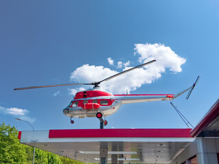 Old Russian helicopter in red silver colors on the roof of a gas station in sunshine and blue sky with white clouds