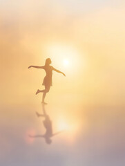 Fototapeta premium Silhouette of a woman gracefully balancing on one foot in a soft, golden light with her reflection on a smooth surface