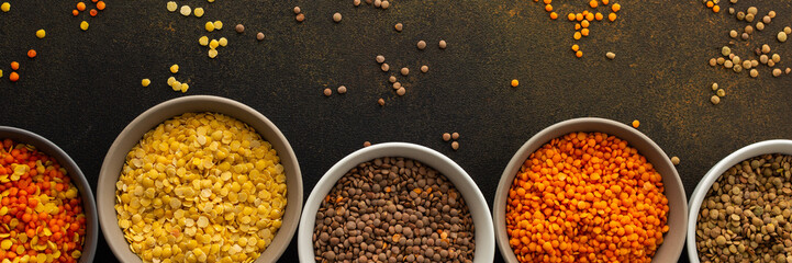 Multi-colored lentils in bowls banner, scattered yellow and brown, green and orange lentils, healthy legumes, top view