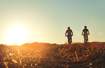 Fototapeta premium Sunset, men and friends on bicycle together with grass, exercise and adventure trail in nature. Cycling race, fitness and people with mountain bike in evening for outdoor workout, energy and health