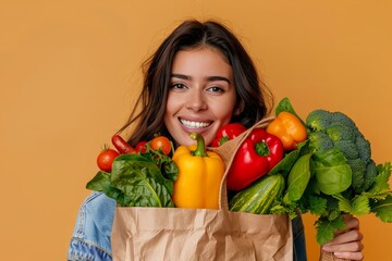 Young smiling cheerful happy cheerful vegetarian woman 20 years old in casual clothes holding paper bag with vegetables after shopping looking at camera over isolated background. 