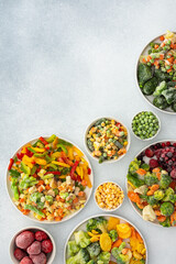 Preparing fresh vegetables in summer for winter, various frozen vegetables and berries in plates on a gray background, top view, copy space