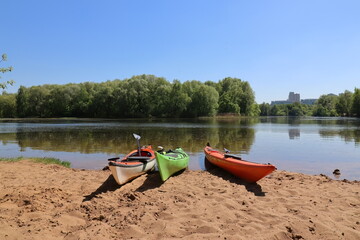 Three kayaks are standing on the sandy bank of the river.
