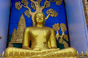 Obraz premium Buddha statue in Nepal. Golden Buddha religious statue in the sacred place temple of Nepal, Asia. Golden Buddha statue adorned with red flowers, sitting serenely meaning peace and tranquility