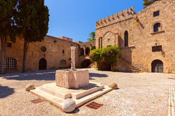 Panoramic view of medieval courtyard with stone buildings and a column in Rhodes, Greece