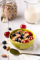 On the bright table a breakfast cup with crunchy wholemeal oat flakes, fresh seasonal fruit and a carafe with organic vegetable drink.