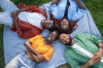 Happy group of african american young friends lying on plaid in park head to head together enjoy...