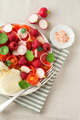 Summer salad with raspberries, cherry tomatoes, fresh radishes, mozzarella cheese and nasturtium leaves. Berries in salads, fruit salty dishes. So French. Natural cotton, farm products, close up