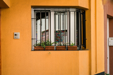 Residential Window with Security Bars and Decorative Plants on an Ocher Facade”