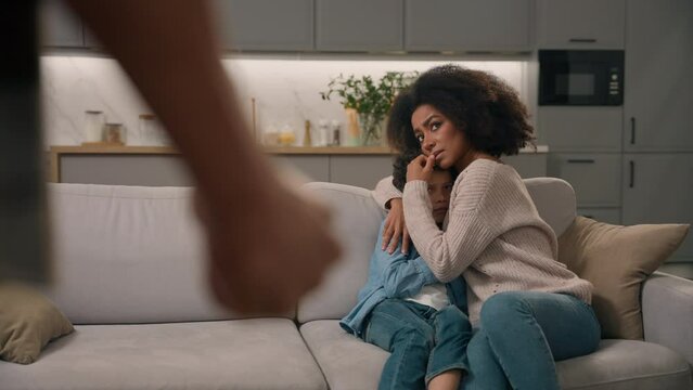 Back view drunk angry unknown African American ethnic man father husband abuser fist beats afraid wife woman hiding little boy child kid son indoors room. Domestic violence marriage harassment problem