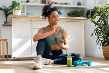 Athletic woman eating a healthy fruit bowl while sitting on floor in the kitchen at home