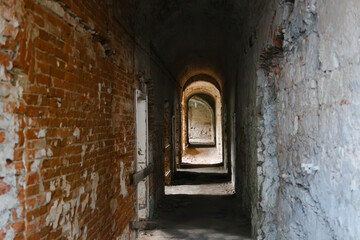 Fototapeta premium Indoor ruined brick premises with arches, doors and corridors. Old abandoned building. Peeling walls. Horror concept. Destroyed internal rooms. Tunnel.