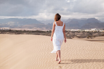 Woman walking along a dune outdoors on a beach with no one around her. Concept: lifestyle, vacation