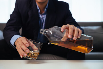 businessman sits and holds glass of liquor in his hand to drink relieve stress after experiencing problems in business. businessman drinking alcohol relieve stress from failed business venture.