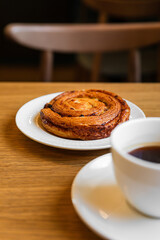 Pain aux raisins, bun with raisins and a cup of coffee on wooden table