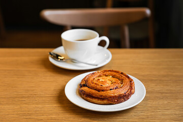 Pain aux raisins, bun with raisins and a cup of coffee on wooden table