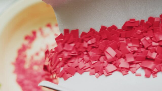 Small pieces of shredded household plastic falling into the container. Close-up.
