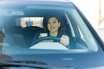Happy woman driving safely with a cup of coffee in her hand during her morning commute