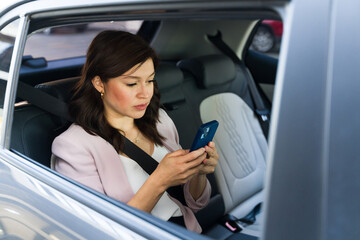 Businesswoman checks her smartphone while sitting in the backseat of a modern vehicle, commuting to work