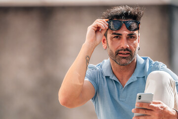 attractive young man with sunglasses looking at his mobile phone on the street outdoors