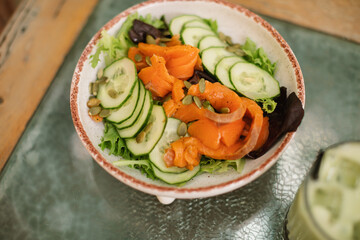 A bowl of lightly salted salmon, cucumber, salad mix and seeds, all seasoned with olive oil. A hearty meal rich in the nutrients.