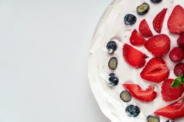 Meringue pavlova cake with whipped cream and fresh berries, strawberries, raspberries and blueberries on a white background. Top view, copy space