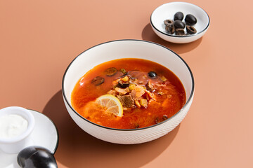 Traditional Meat Solyanka Soup with Olives and Lemon Garnish on Minimalist Background