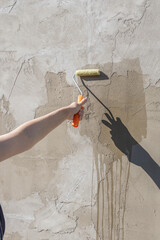 The girl's hand holds a roller dipped in primer and covers the front wall of the house with primer.