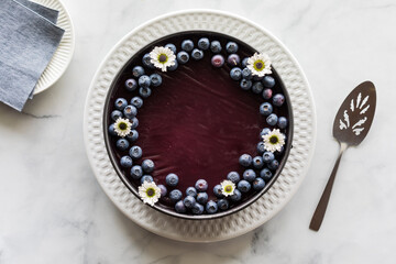 A homemade blueberry cheesecake topped with blueberries and daisy blossoms