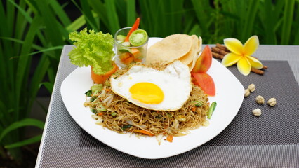 
Fried Vermicelli Mixed with Vegetables Sprinkled with Matasapi Egg, Pickled Cucumber, Salad, Tomatoes and Crackers, This is a Typical Indonesian Food