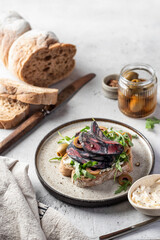Sandwich with salami sausage, grain bread, cream cheese, olives, aragula and microgreens with ingredients on light gray textured background. Breakfast