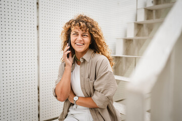 Fototapeta premium Adult woman sit on the stairs and talk on mobile phone