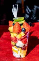 Healthy snak, dessert, colorful fresh fruits and berries cutted in pieces and served in plastic glass, street food