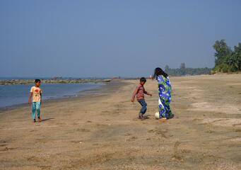 South asian young girl playing football local boys in a sea beach wearing traditional costumes, beautiful asian lady enjoying her vacation by playing beach soccer with local kids
