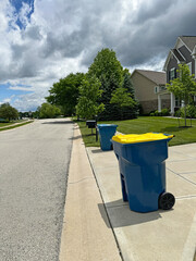 Blue trash cans, including a yellow recycle bin, beside the street on trash day in an Indiana Neighborhood with copy space.