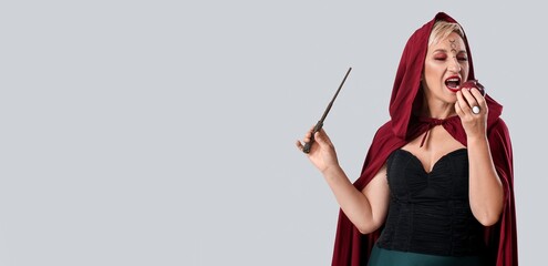 Mature witch with magic wand eating apple on grey background with space for text