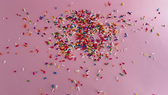 Rainbow sugar sprinkles scattering on pink background