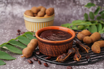 Bowl of tasty tamarind jam and fruits on grey background