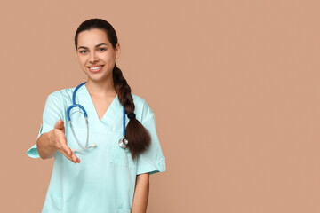 Portrait of female doctor reaching out for handshake on beige background