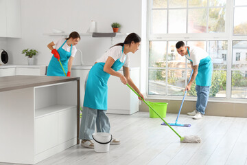 Team of young janitors mopping floor in kitchen