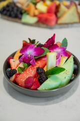 Bowl of colorful fruit salad with exotic fruit berries and melons decorated with purple orchids, Vertical 