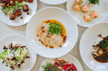 A white plate with a variety of food items including pasta, vegetables, and fruit. The plate is set on a table with other plates of food. From above.