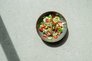 A bowl of salad with strawberries, cucumbers, and onions photographed from above. Room for copy.